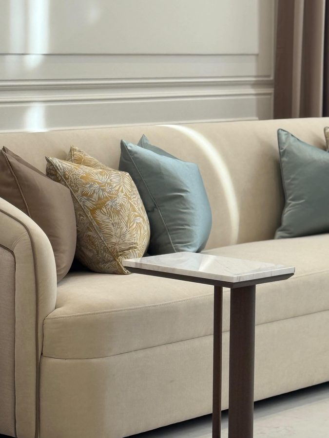 Cream sofa with sage and gold cushions beside a slim side table