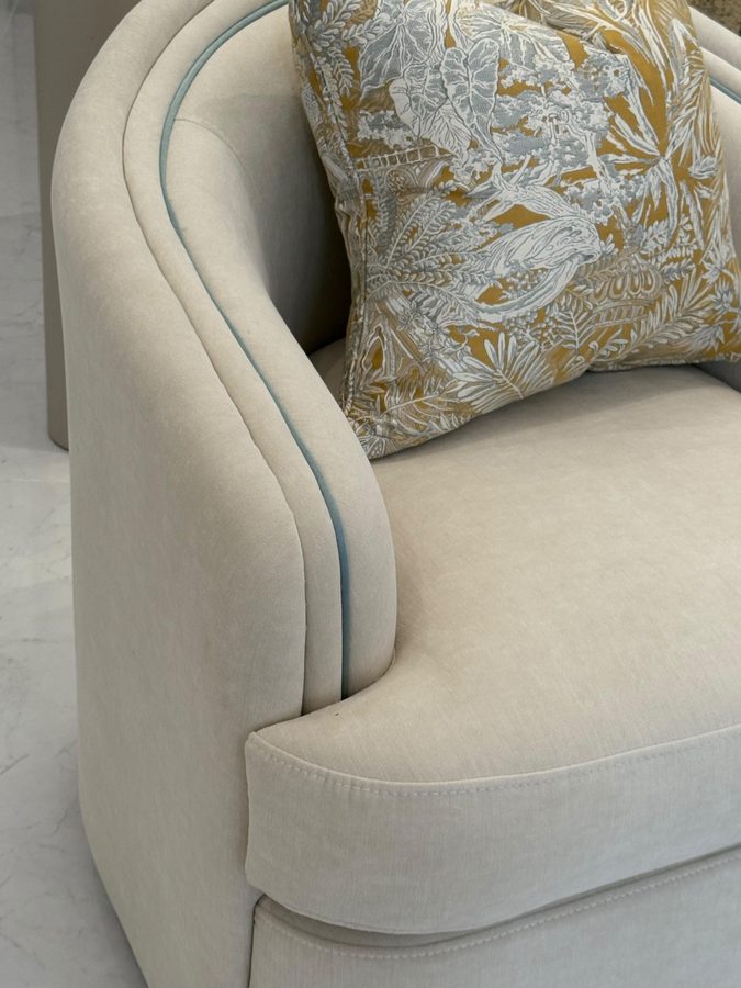 Curved armchair with contrast piping and a paisley cushion