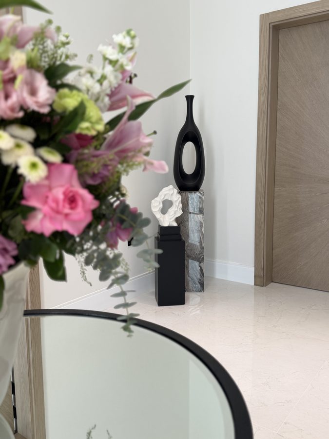 Entrance with flowers and a sculpture beside a timber door